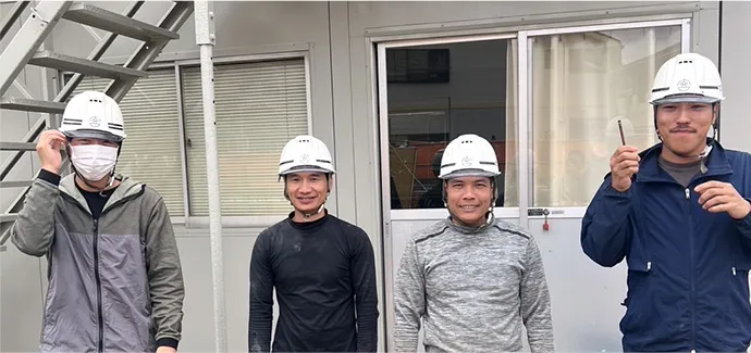 プレハブの前でポーズをとる4人の作業員